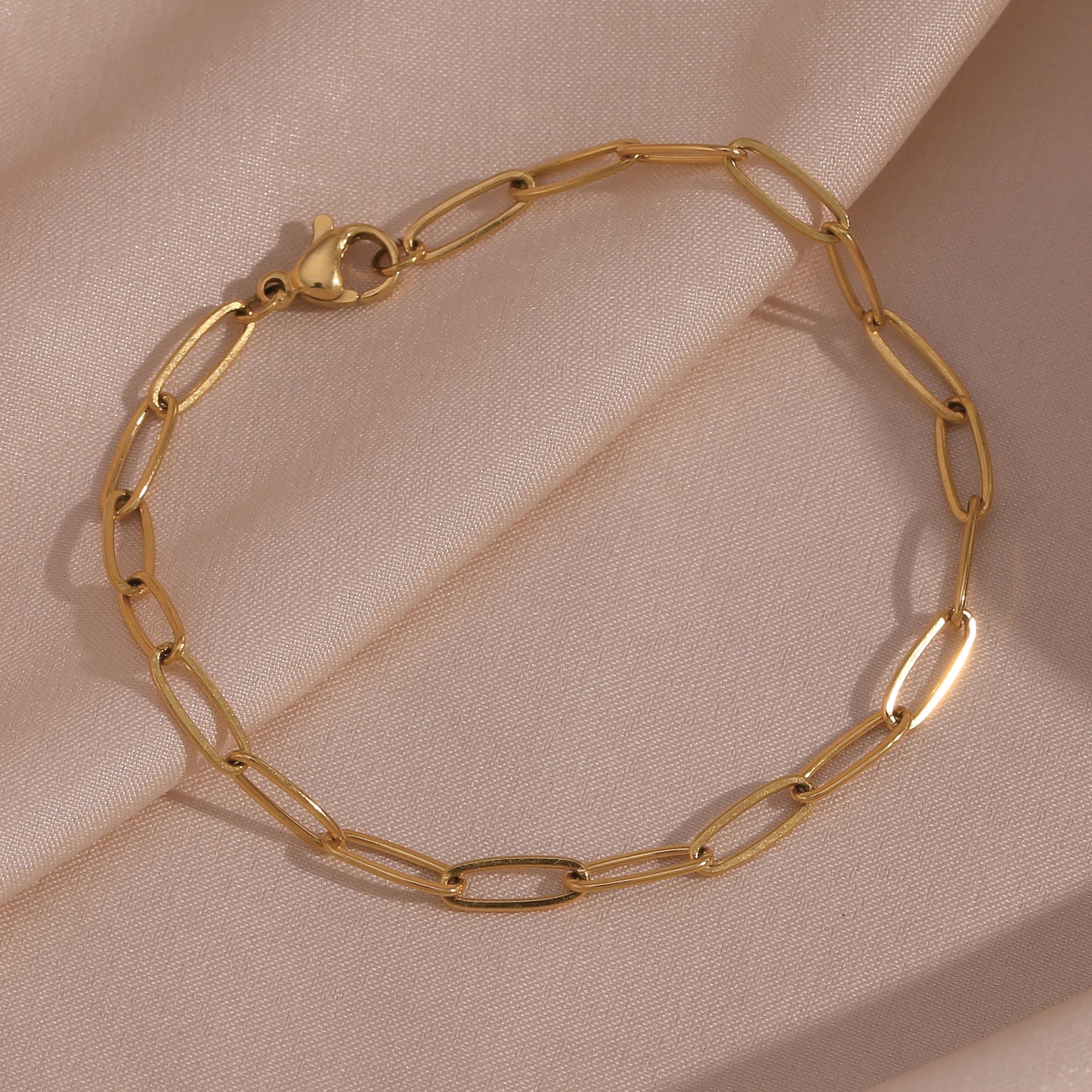 Gold paperclip chain bracelet on a beige fabric background