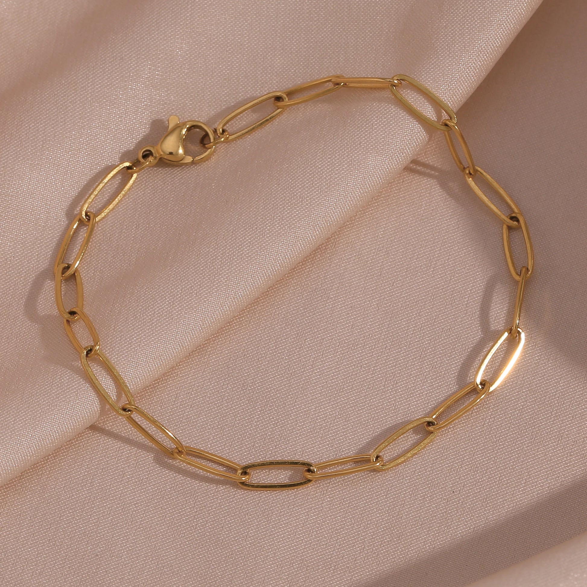Gold paperclip chain bracelet on a beige fabric background