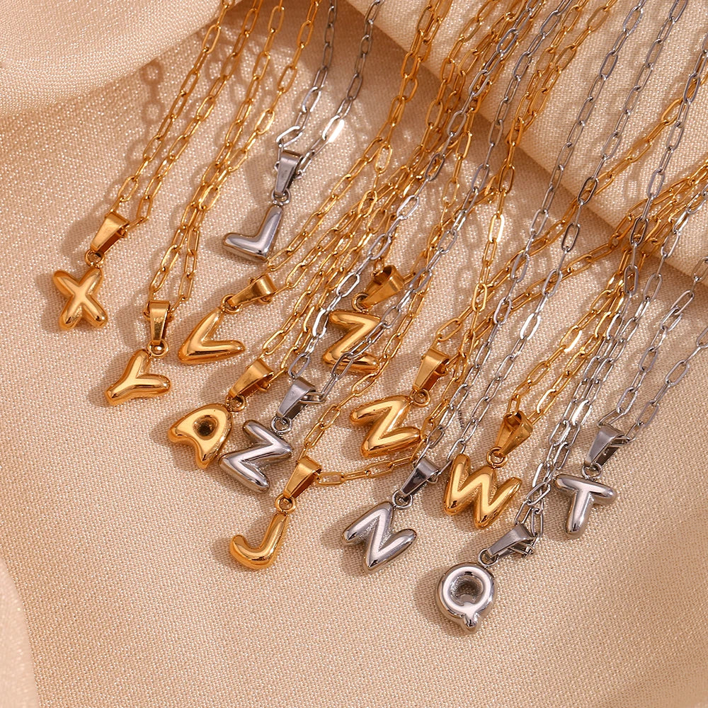 Collection of gold and silver necklaces with letter pendants on a beige fabric background