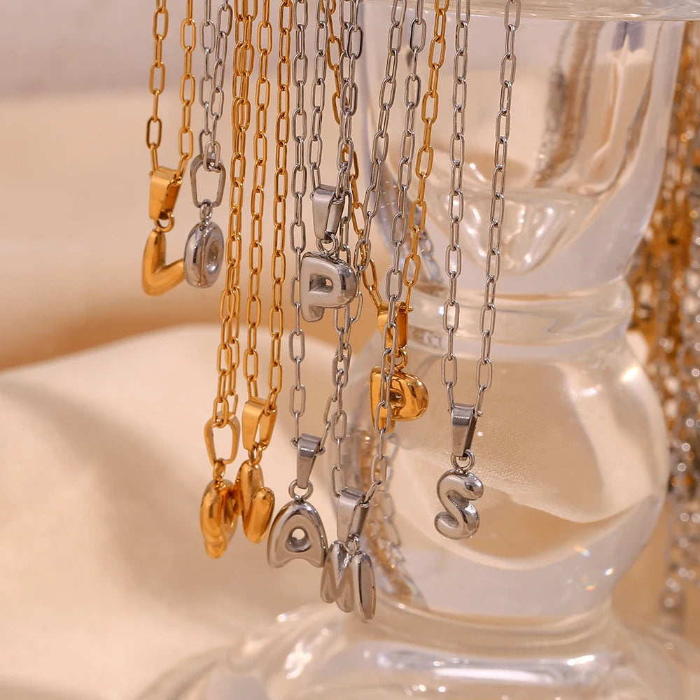 Gold and silver necklaces with letter pendants on a clear stand.