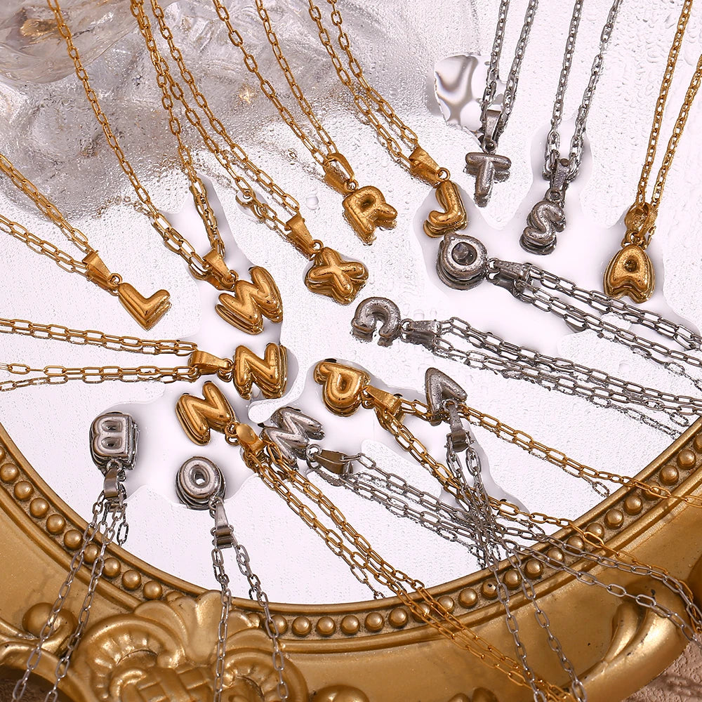 Collection of gold and silver necklaces with letter pendants on a decorative surface.