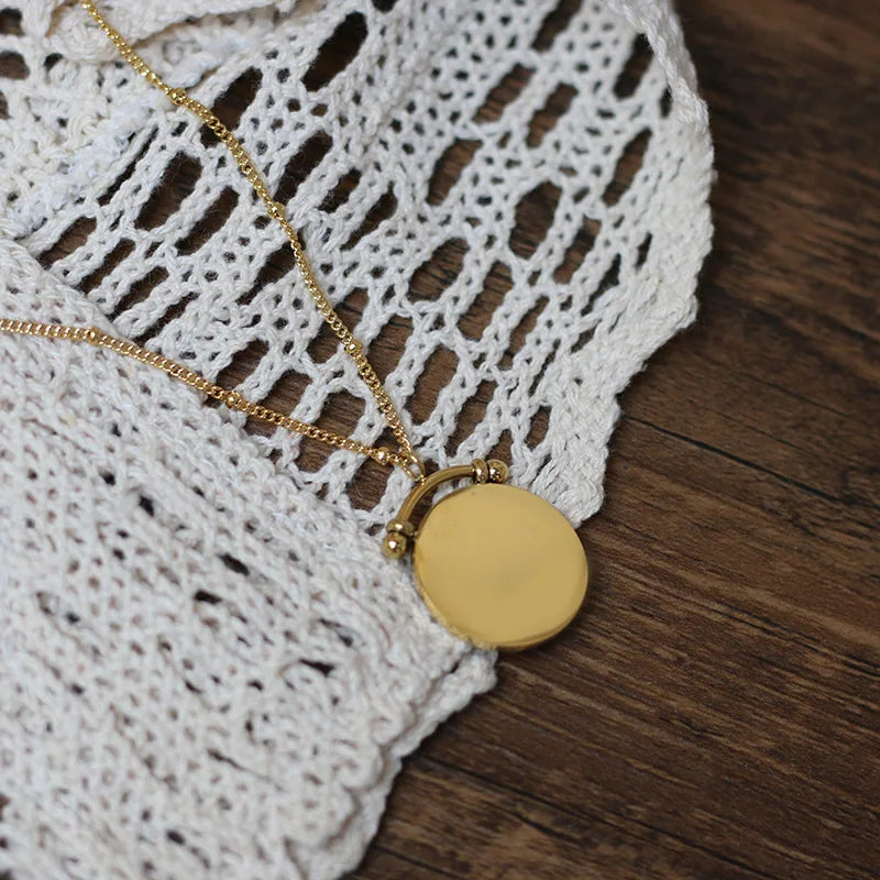 A double layered stainless steel necklace with a gold sun symbol pendant on a shorter chain and a mandala pendant on a longer chain, both made of stainless steel with gold plating.
