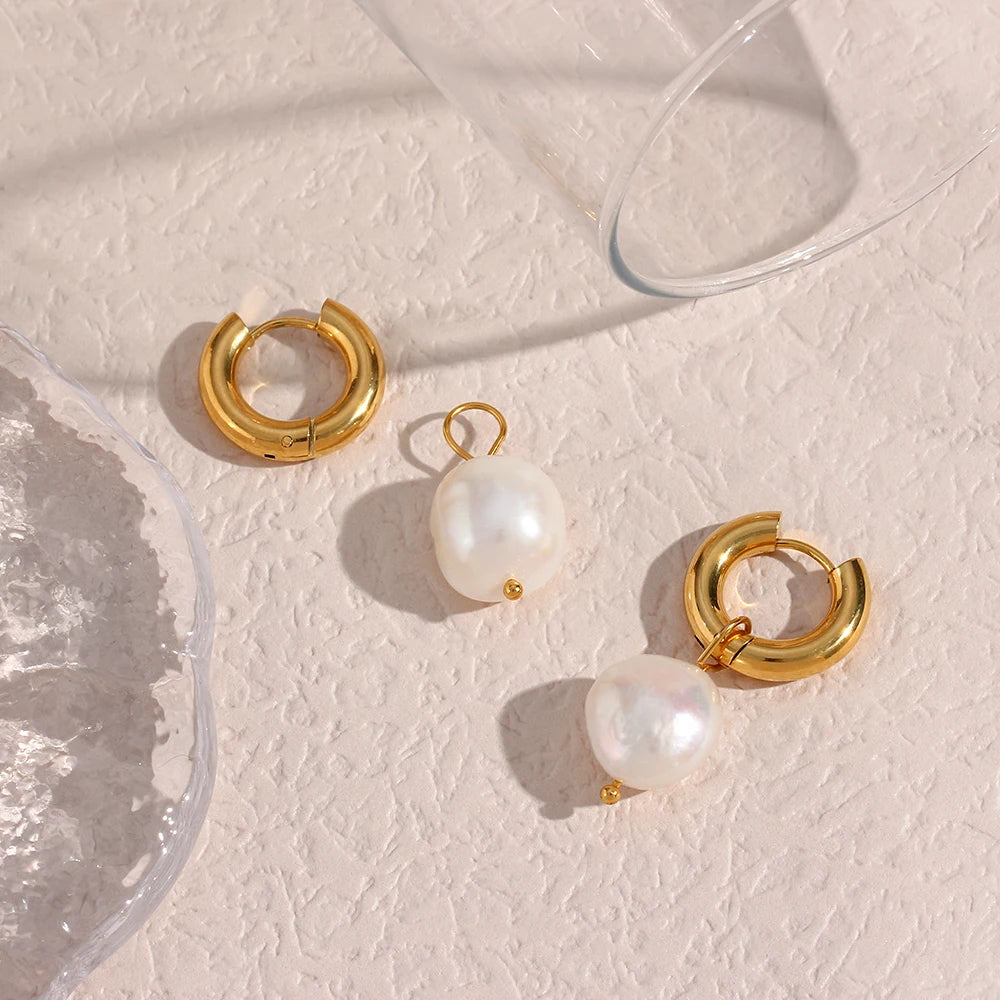 Gold hoop earrings with pearl drops on a textured beige surface