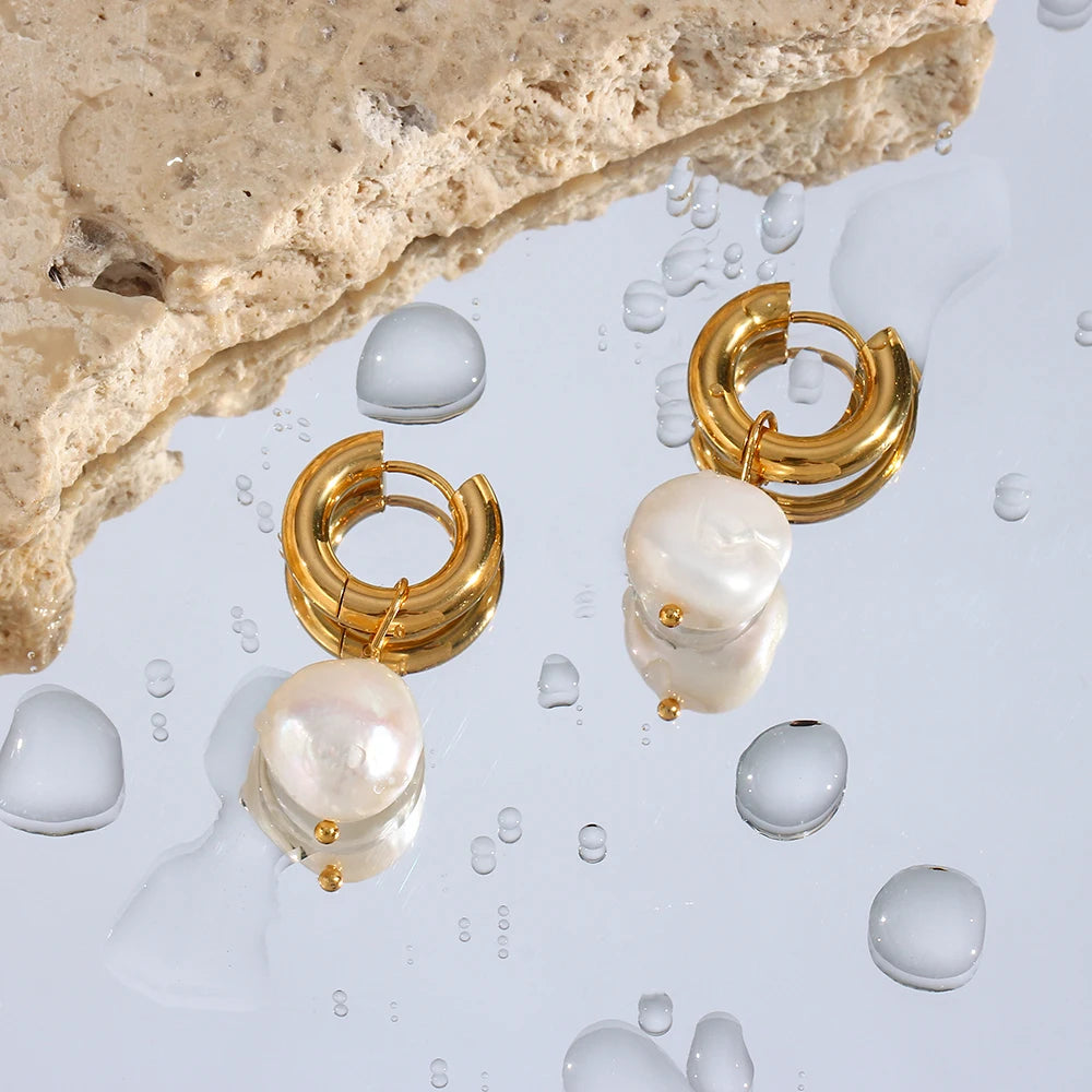 Gold hoop earrings with pearl-like stones on a water droplet background
