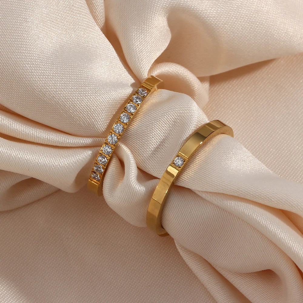 Two gold rings with diamond accents on a beige fabric background