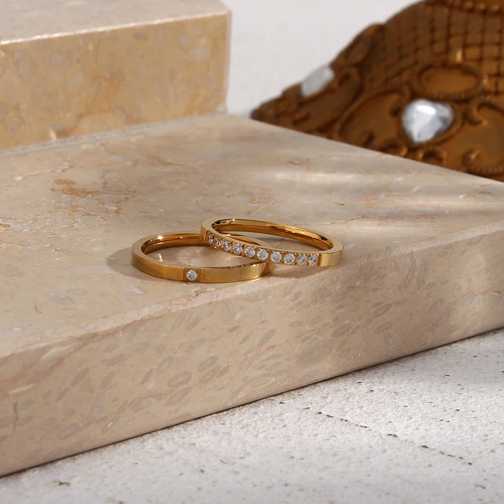 Two gold rings with small diamonds on a marble surface