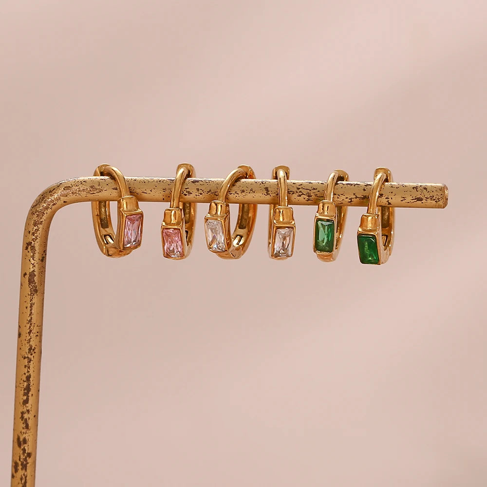 Sets of gold hoop earrings with gemstone accents on a beige stand.