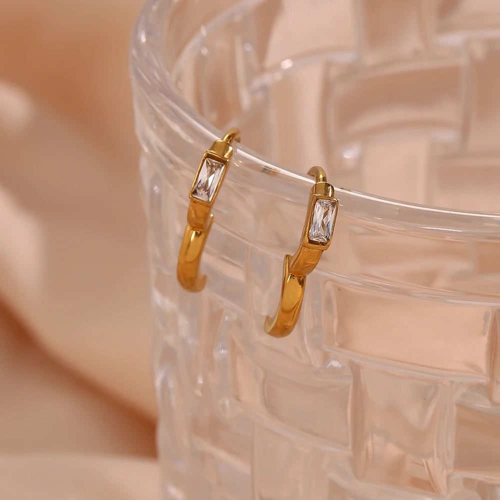 Gold hoop earrings with clear stones on a textured beige surface