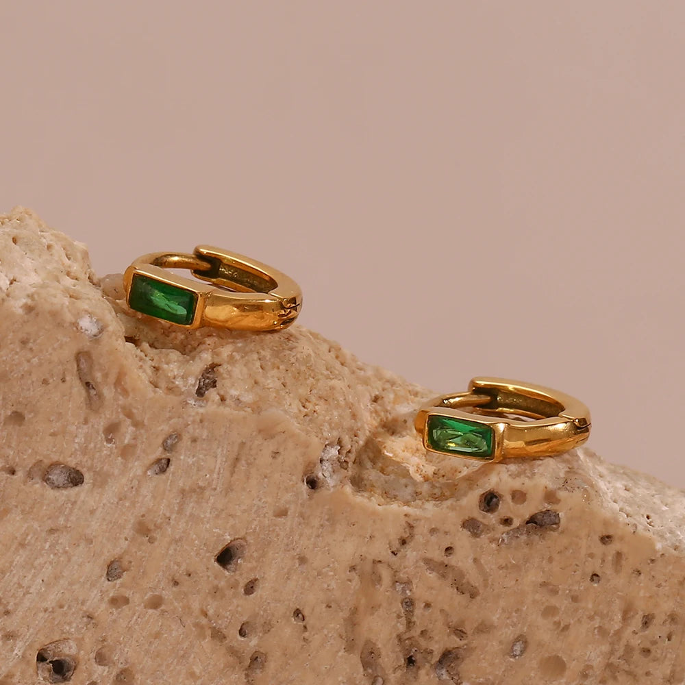 Gold hoop earrings with green gemstones on a textured beige surface