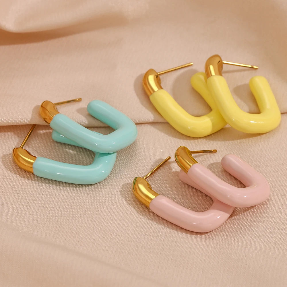 A pair of gold-colored hoop earrings with a pastel coatings, displayed on fabric.