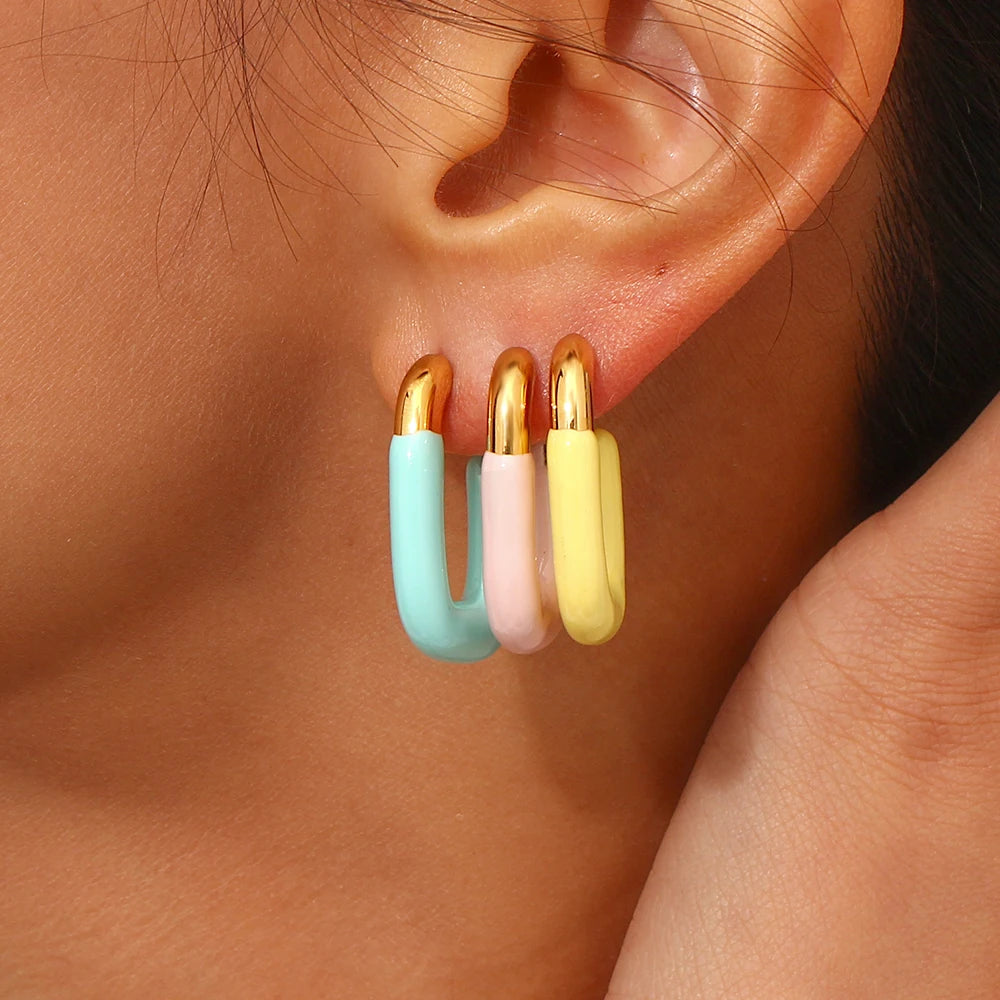 A pair of gold-colored hoop earrings with a pastel colored coating in model's ear.