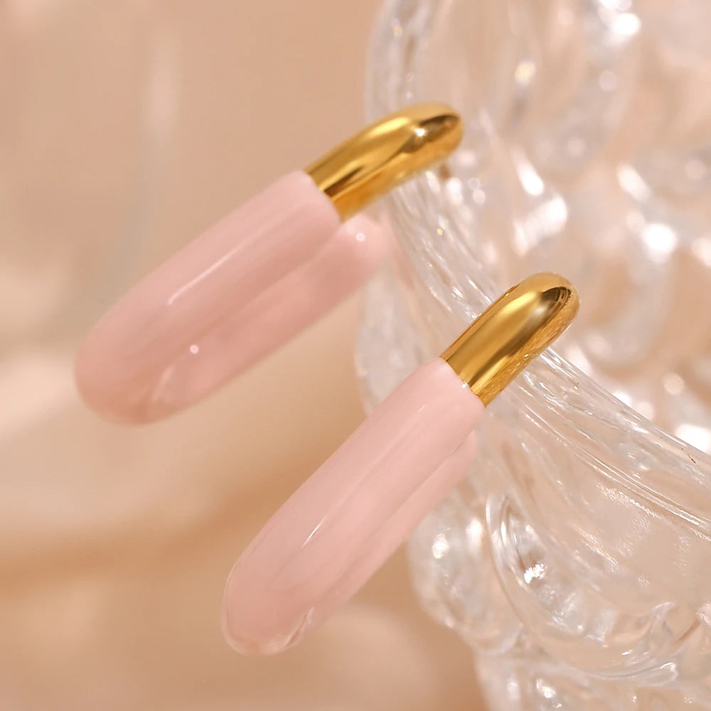 A pair of gold-colored hoop earrings with a pastel pink coating.