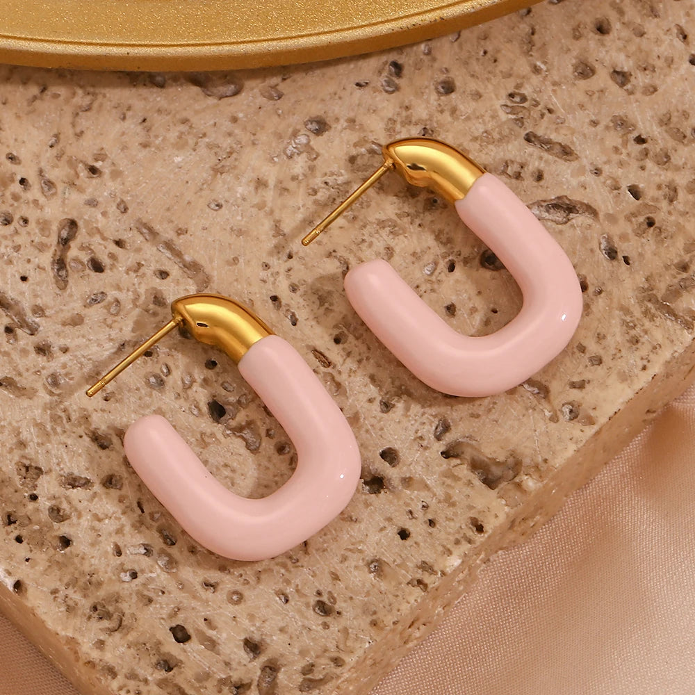 A pair of gold-colored hoop earrings with a pastel pink coating.