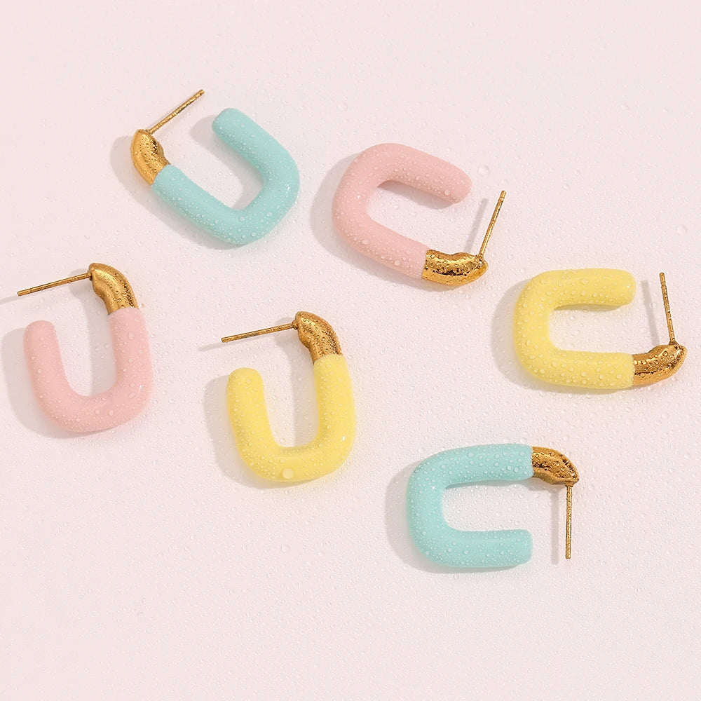 A pair of gold-colored hoop earrings with a pastel colored coating on white background.