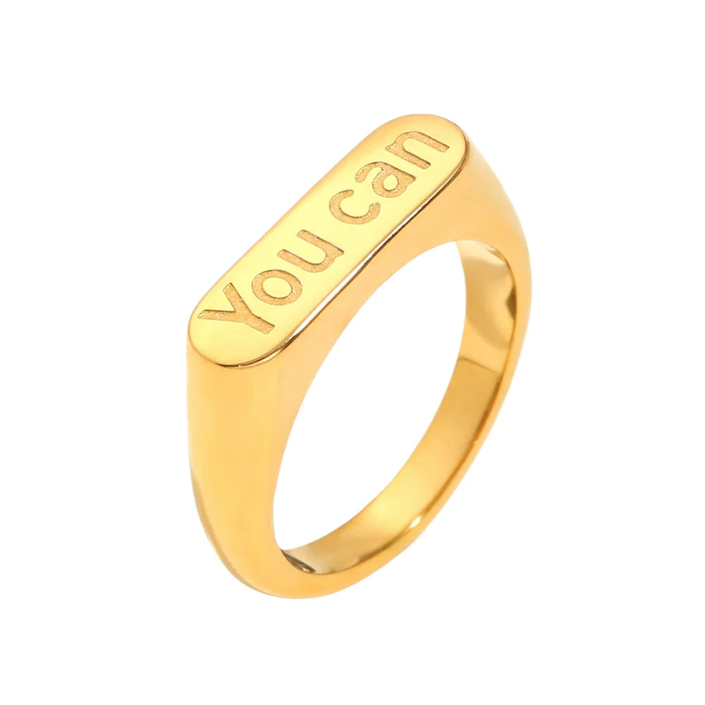 A gold stainless steel signet ring with the words 'you can' engraved on the top.