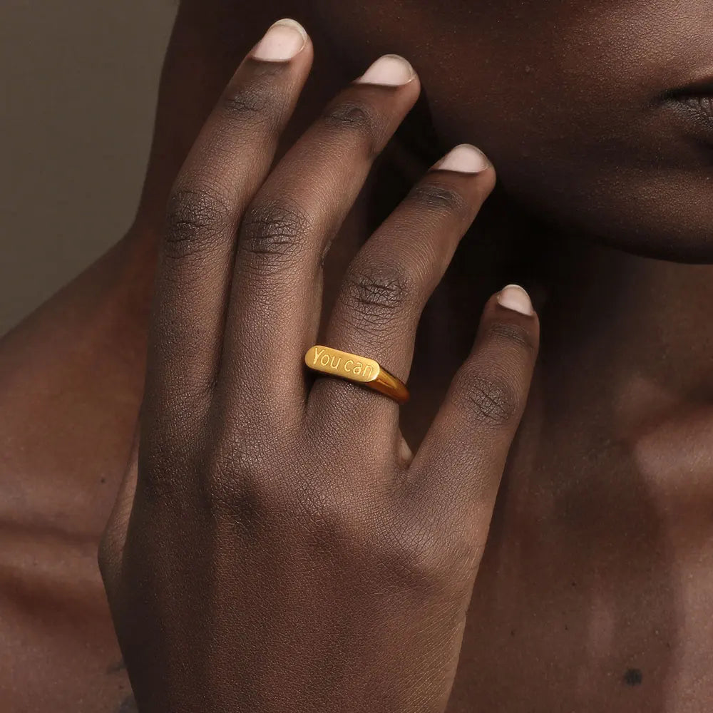 A stainless steel signet ring with the word 'you can' engraved on the top. on a model's finger