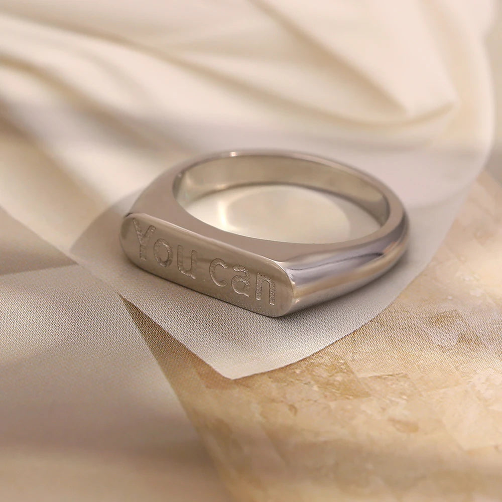 A stainless steel signet ring with the word 'you can' engraved on the top.