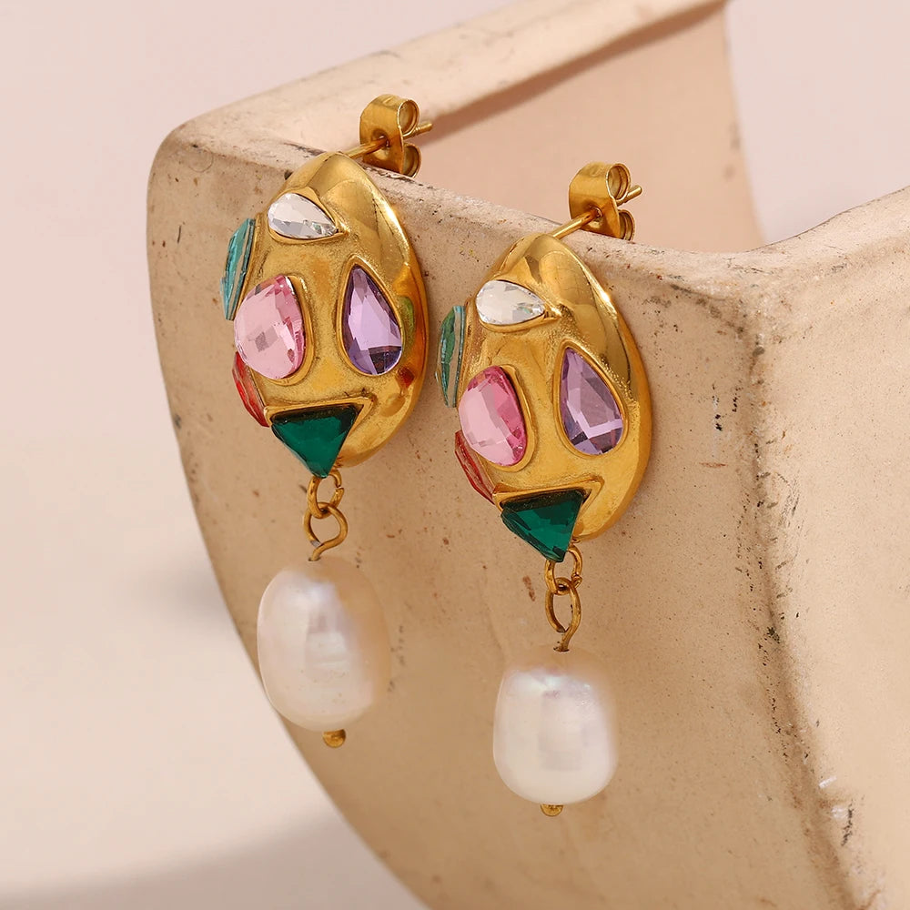 Gold earrings with colorful gemstones and pearl drops on a beige stone surface