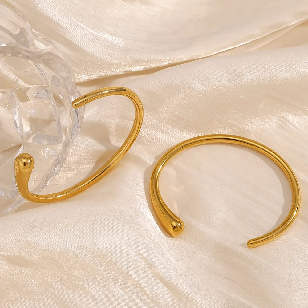 A gold steel bangle bracelet with a sleek, minimalist design, displayed against a satin fabric