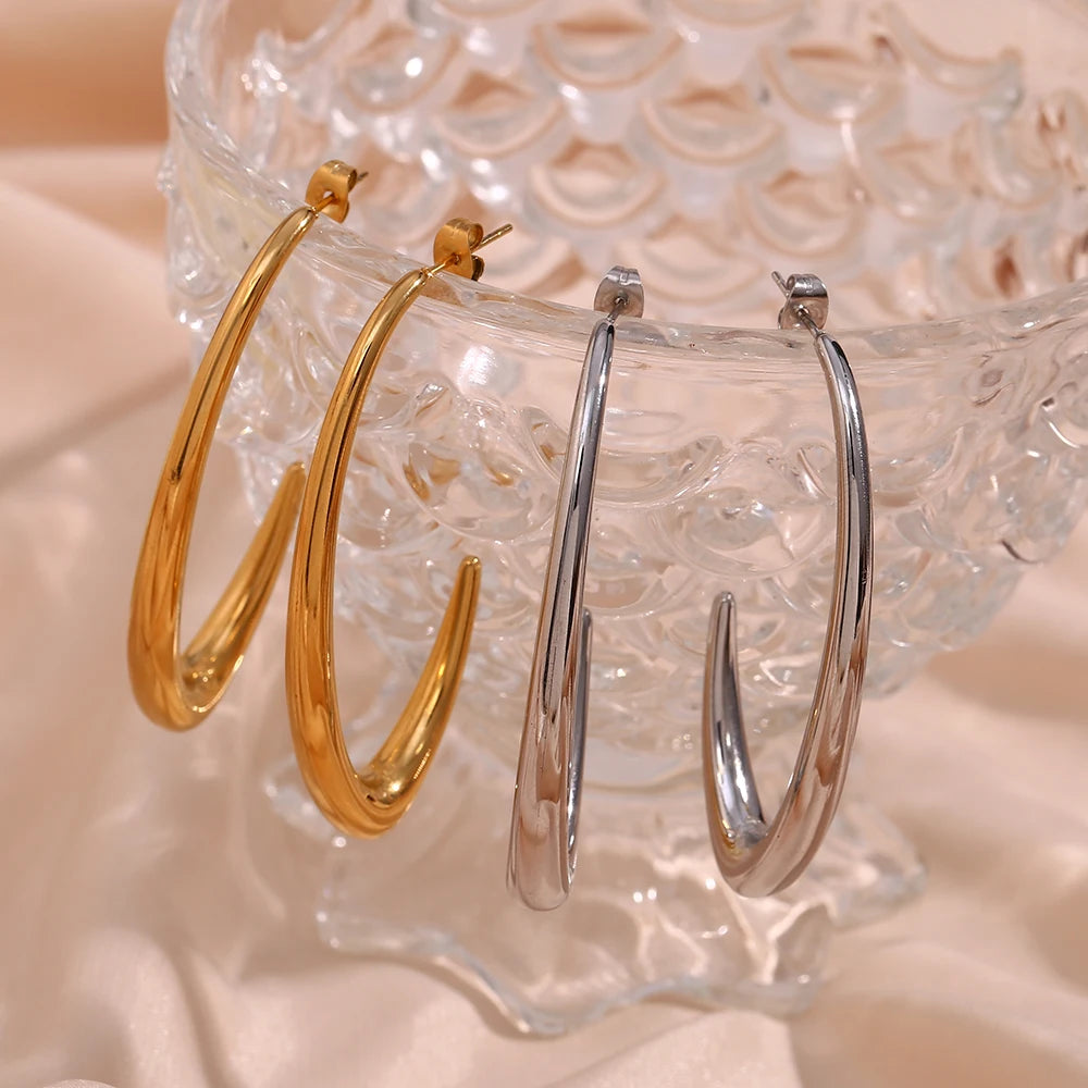 Two pairs of elegant large Hoop Earrings, presented on a textured stone surface. The earrings are designed in a bold, minimalist style.