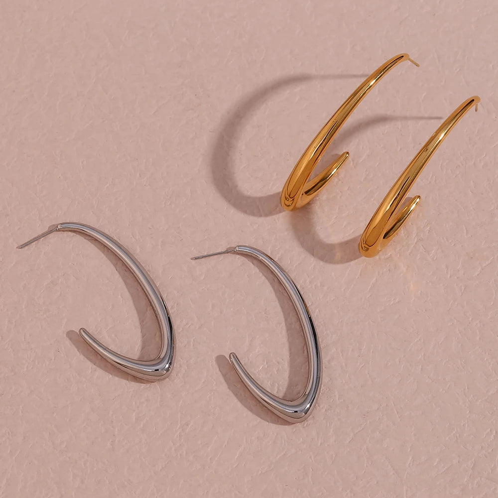 Two pairs of elegant large Hoop Earrings, presented on a textured stone surface. The earrings are designed in a bold, minimalist style.
