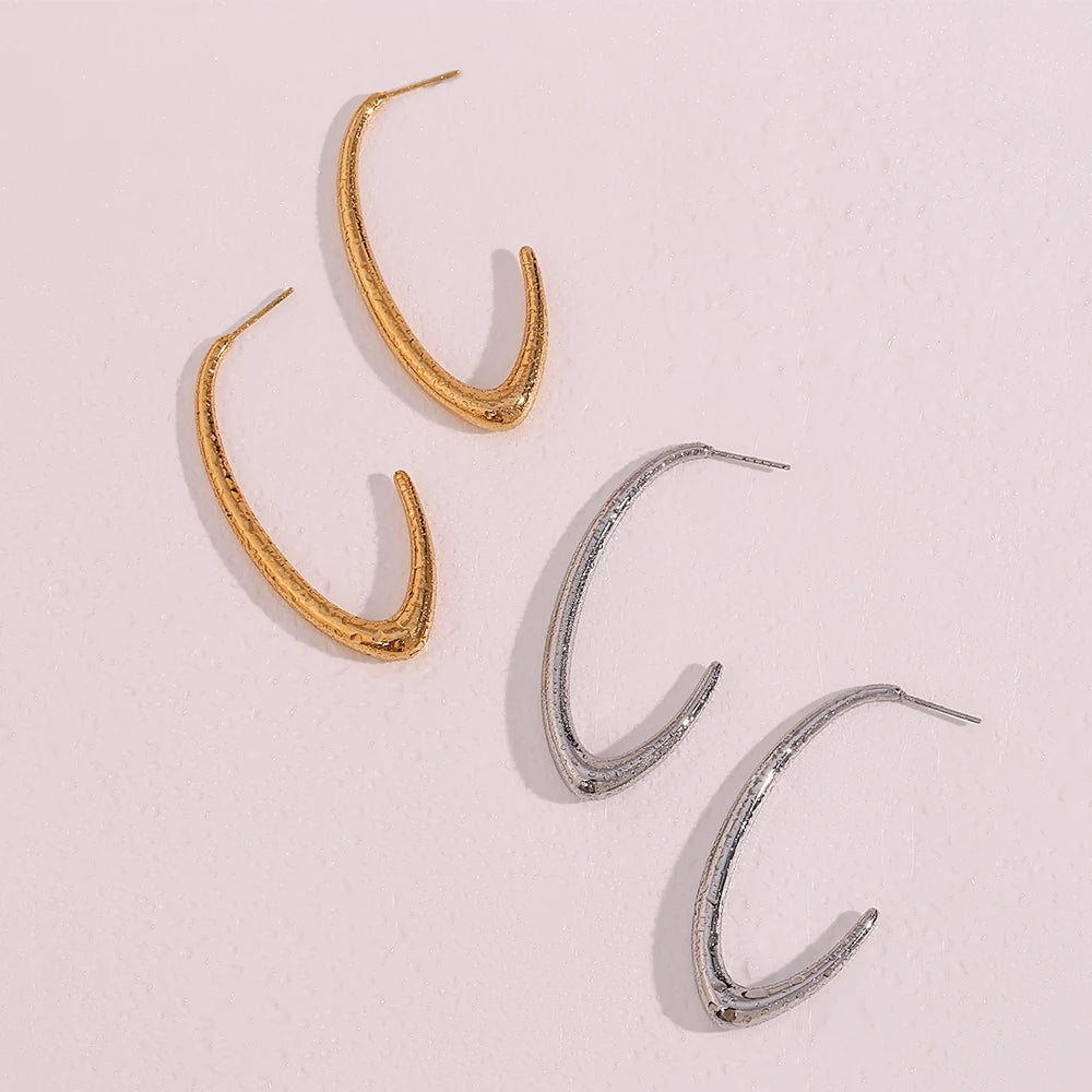 Two pairs of elegant large Hoop Earrings, presented on a textured stone surface. The earrings are designed in a bold, minimalist style, wet