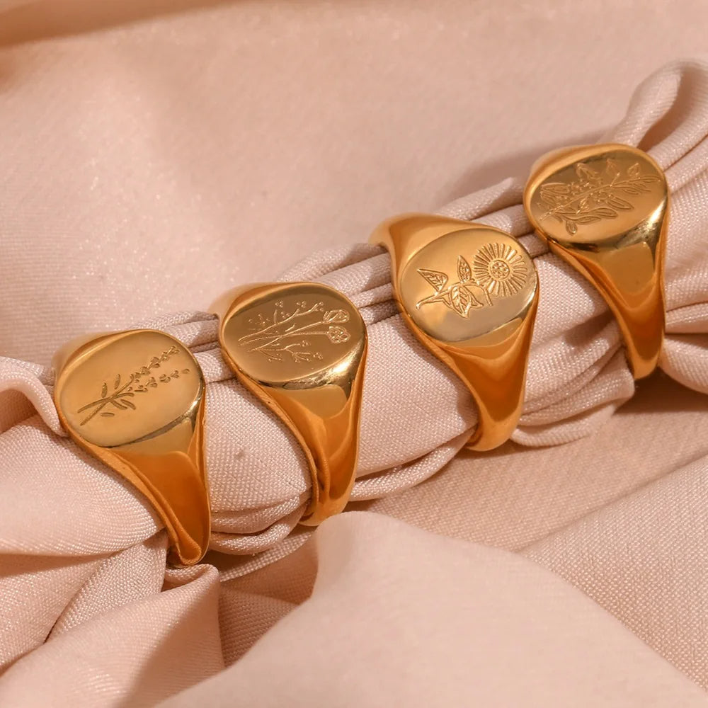 Four gold rings with engraved designs on a pink fabric background