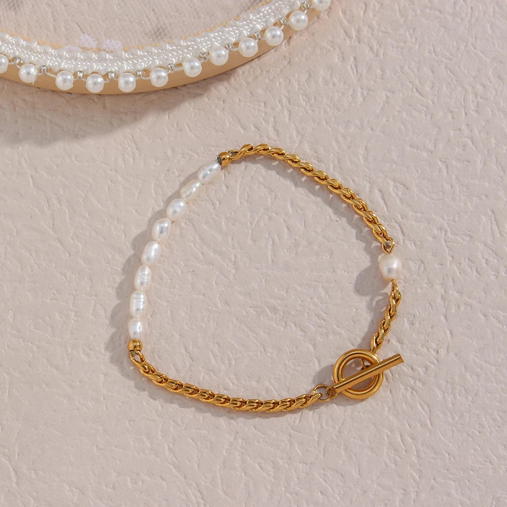 A gold bracelet with twisted chain design and pearl accents, displayed on a beige fabric surface.