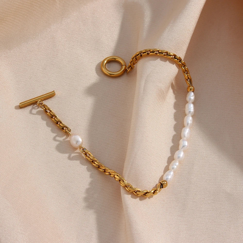 A gold bracelet with twisted chain design and pearl accents, displayed on a beige fabric surface.