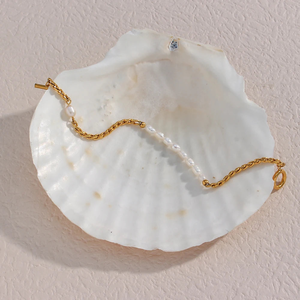 A gold bracelet with twisted chain design and pearl accents, displayed on a beige fabric surface.