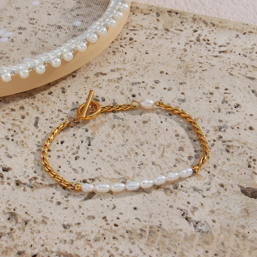A gold bracelet with twisted chain design and pearl accents, displayed on a beige fabric surface.