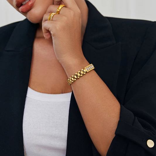 Person wearing a black blazer and gold bracelet on a neutral background