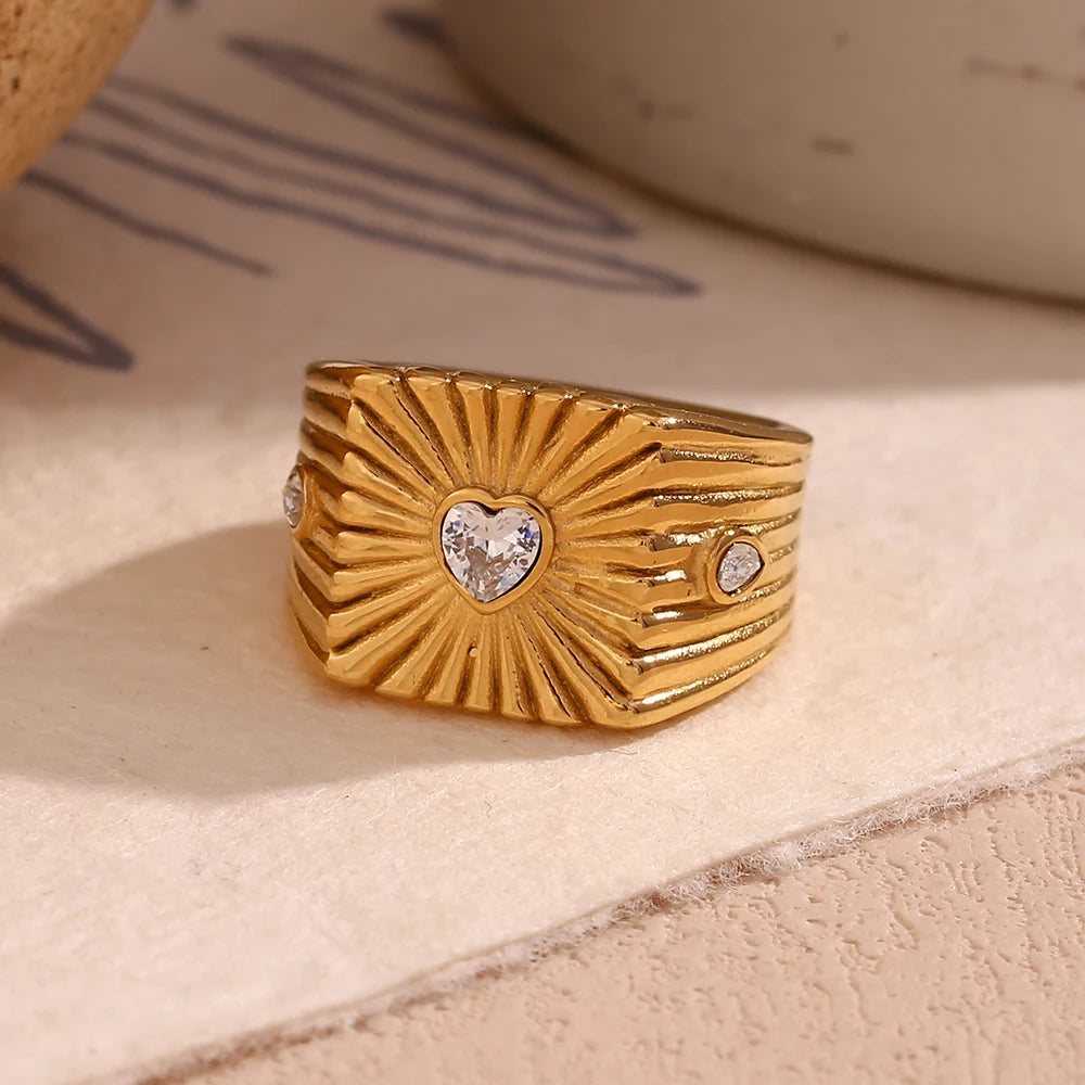 A gold stainless steel signet ring with a geometric design and crystal accents, featuring a prominent heart shaped zirconia at the top.