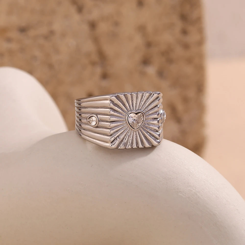 A  stainless steel signet ring with a geometric design and crystal accents, featuring a prominent heart shaped zirconia at the top.