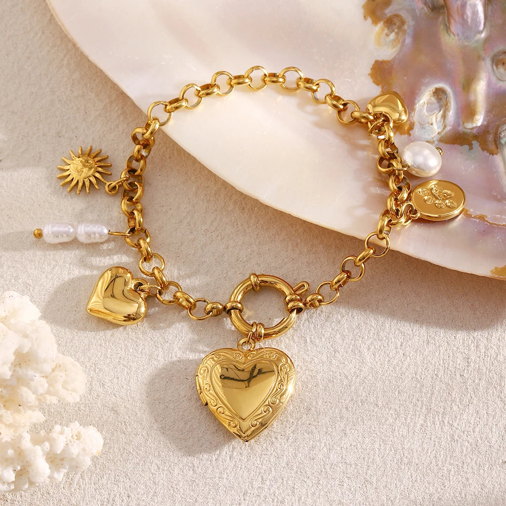 Gold bracelet with heart-shaped locket and pearl and pet paw charms, on a beige surface
