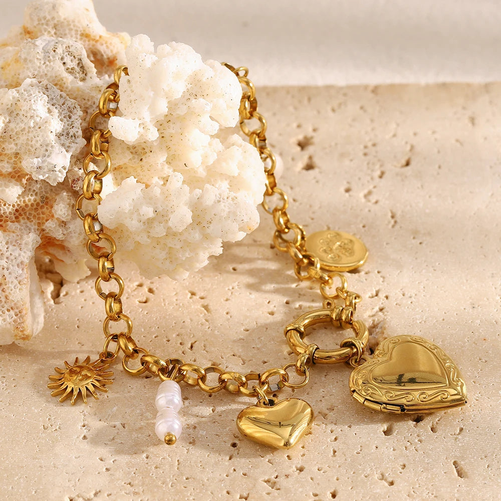 Gold charm bracelet with heart and sun designs on a sandy background
