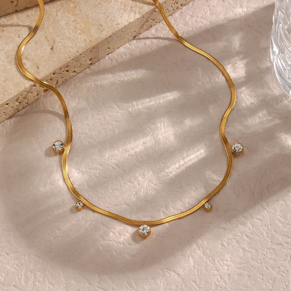 A 18K gold-plated stainless steel necklace with round zirconia crystals, on a beige background.