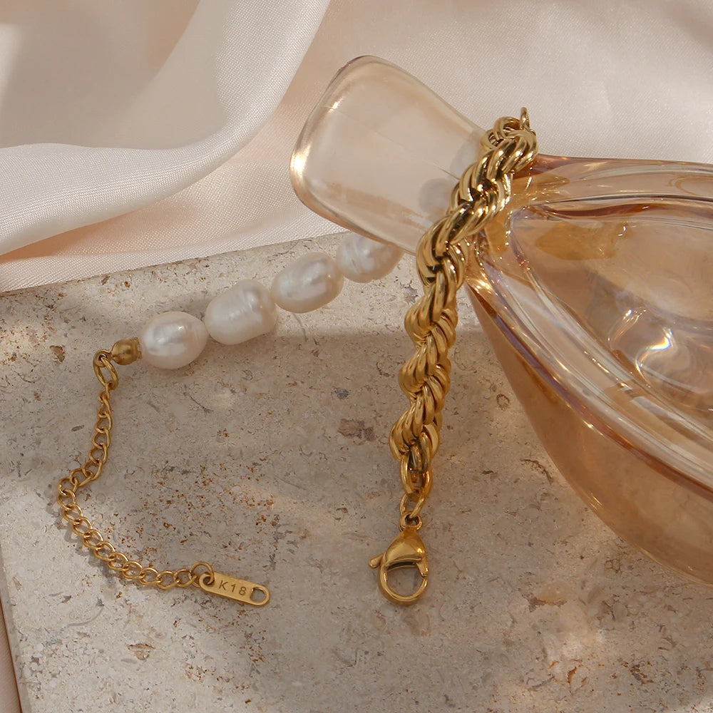 Gold bracelet with a clasp on a textured surface next to a perfume bottle.