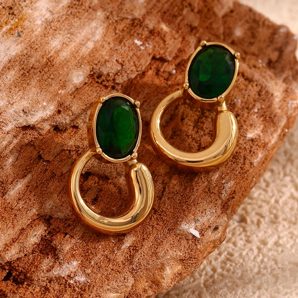 A pair of gold-colored earrings with deep green or black oval stones set in a loop design on wooden display