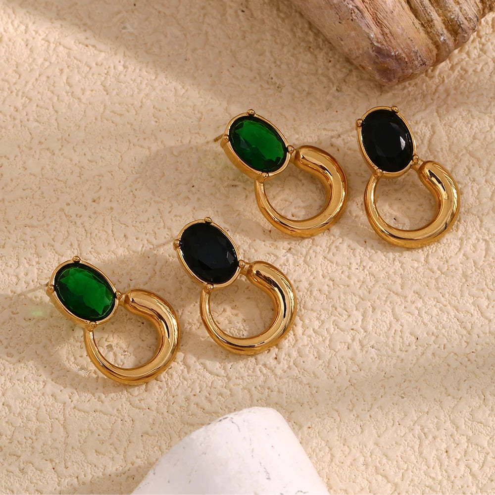 A pair of gold-colored earrings with deep green or black oval stones set in a loop design flat lay