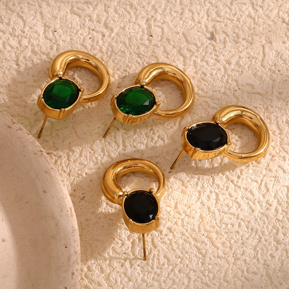 A pair of gold-colored earrings with deep green or black oval stones set in a loop design on display