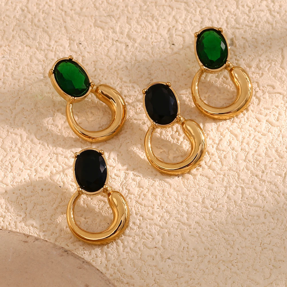 A pair of gold-colored earrings with deep green or black oval stones set in a loop design flat lay