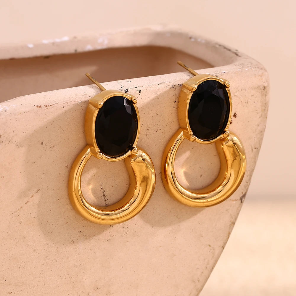 A pair of gold-colored earrings with deep green or black oval stones set in a loop design on display