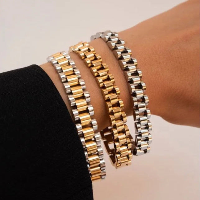 Three gold and silver link bracelets on a wrist against a neutral background