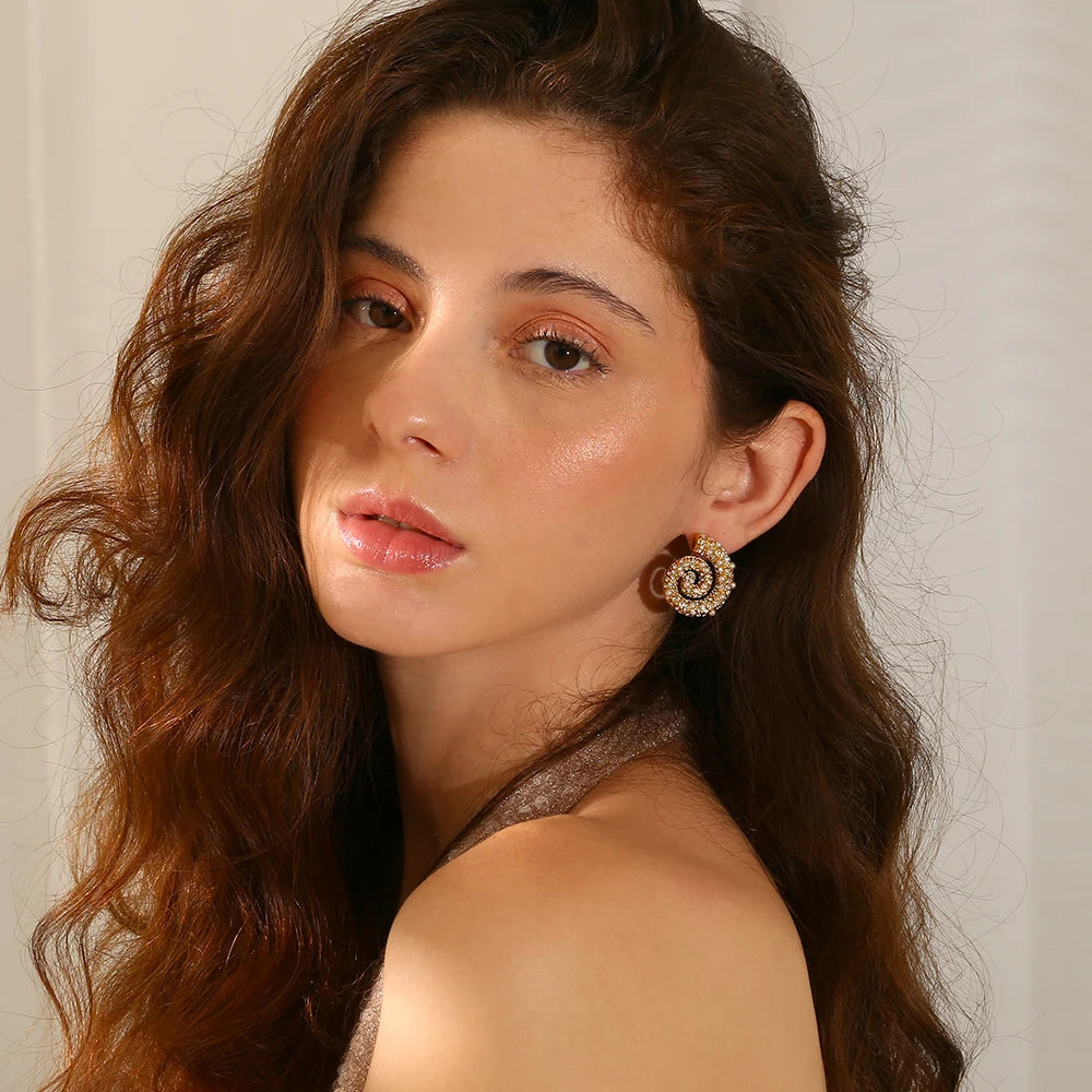 A pair of spiral design earrings adorned with pearls and zirconias, set in gold-plated metal, shown on model