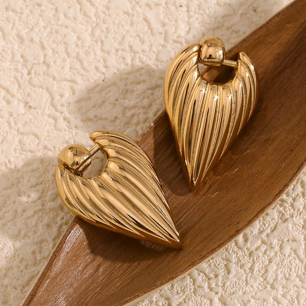 A pair of golden point earrings with a textured design, attached to a wooden background