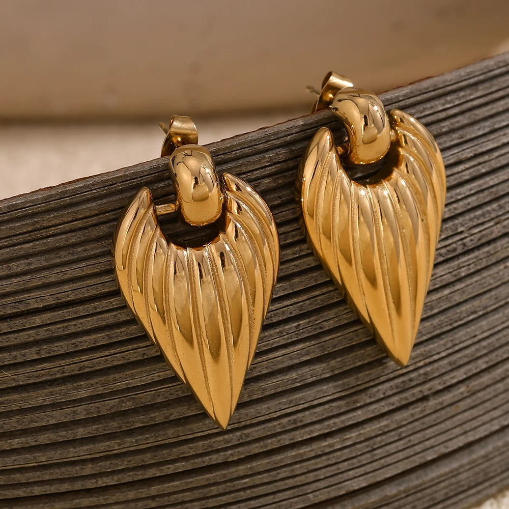 A pair of golden point earrings with a textured design, hanging from a tectured backdrop object
