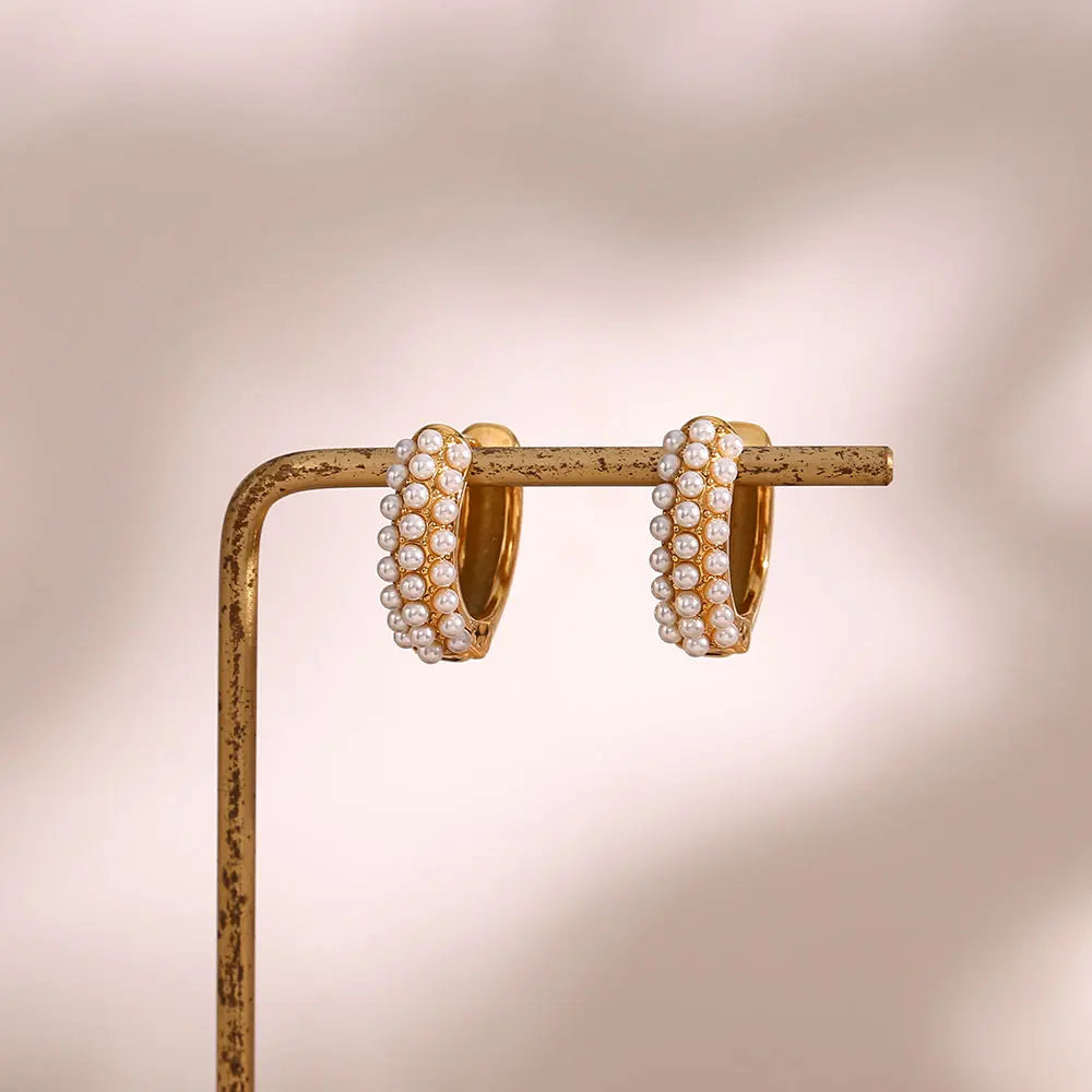 Gold hoop earrings with pearl accents on a stand against a soft beige background
