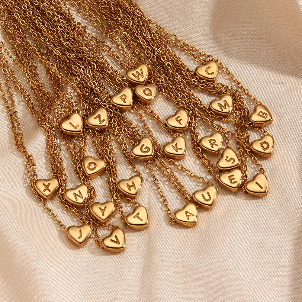 Gold necklaces with heart-shaped pendants displaying initial letters on a beige fabric background