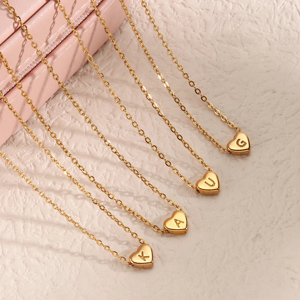 Gold heart-shaped initial pendants on gold chains against a light pink background
